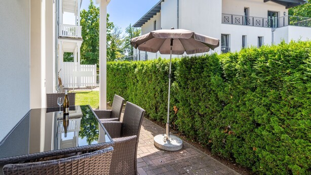 A patio with a glass table, wicker chairs, and a large umbrella. - Villa Waldschloss, app. 01 (Heringsdorf)