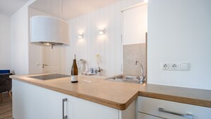 A modern kitchen with a wooden countertop, built-in cabinets, a stainless steel sink, and a wine bottle. - Villa Waldschloss, app. 01 (Heringsdorf)