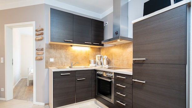 Una cocina moderna con armarios oscuros, horno empotrado y refrigerador de acero inoxidable.
