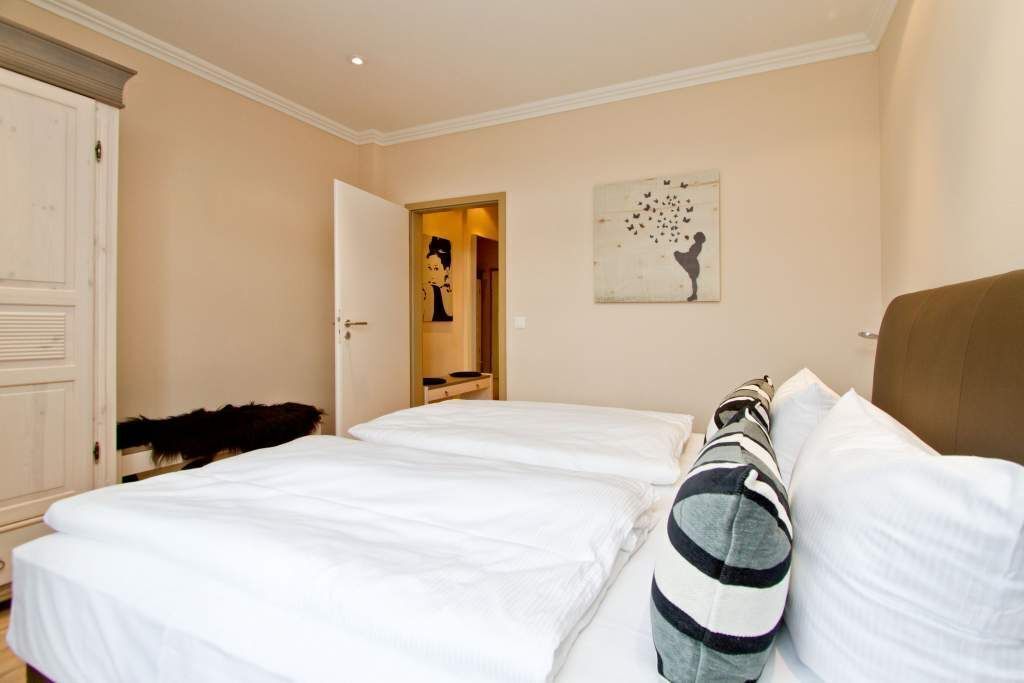 A hotel room with two beds, a wardrobe, a mirror, and a wall art piece.