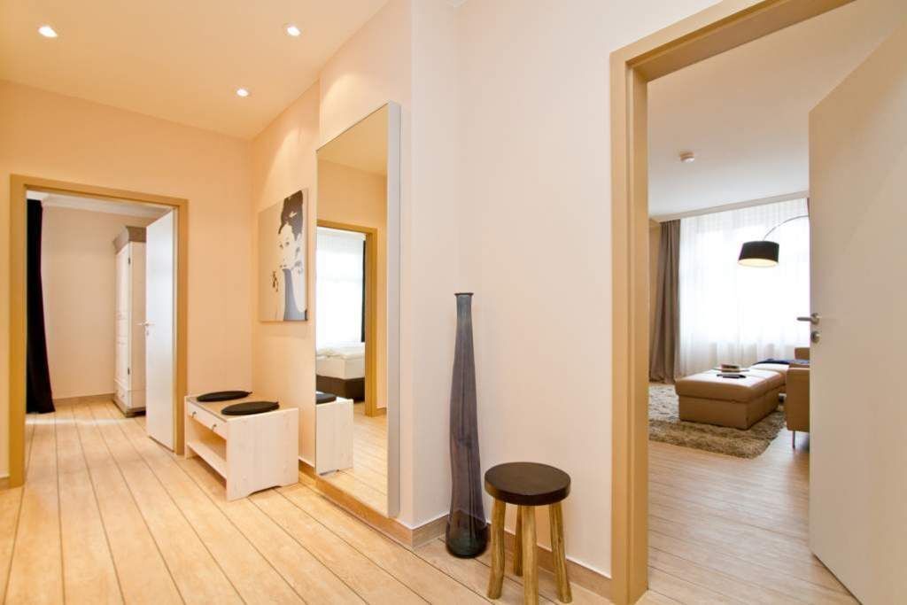 Quarto de hotel moderno com piso de madeira, um espelho grande, mesa de cabeceira e vista para a sala de estar.