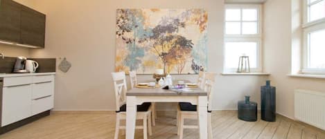 A modern kitchen with a dining table set for four, a large abstract painting on the wall, and a window providing natural light.