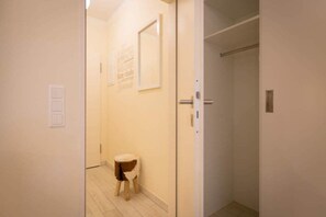 Un pasillo estrecho con un taburete pequeño, una puerta con un espejo y una pared con un cartel de bienvenida.