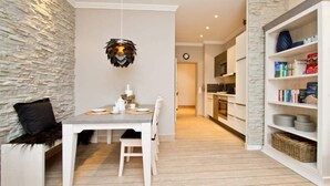 Eine moderne Küche mit weißen Schränken, einer Wand mit Steinverkleidung und einem Essbereich mit weißem Tisch und Stühlen.