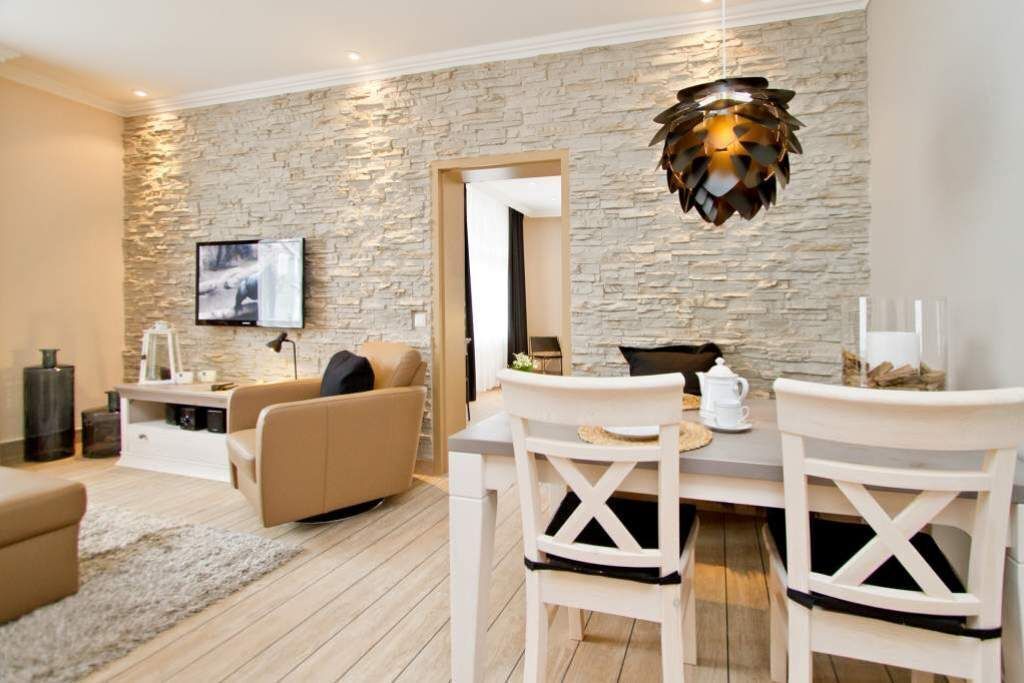 A modern living room with a stone wall, a flat-screen TV, a dining table with chairs, and a fireplace.