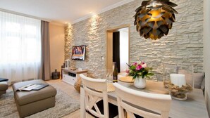 A modern living room with a stone wall, a dining table with chairs, a sofa, and a television mounted on the wall.