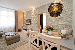 Ein modernes Wohnzimmer mit Steinwand, einem Esstisch mit Stühlen, einer Couch und einem an der Wand befestigten Fernseher.