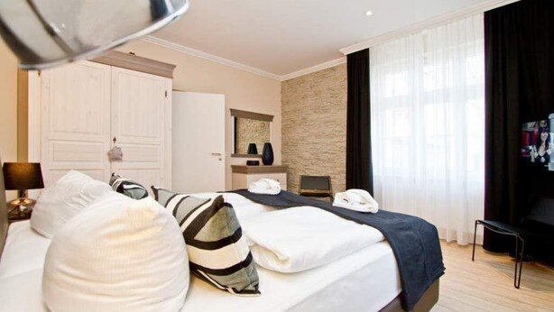 A hotel room with a large bed, a wardrobe, a mirror, a desk, and a chair.