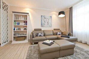 Una sala moderna con un sofá modular, un reposapiés pequeño, una estantería y una lámpara de pie.