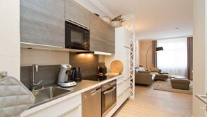 A modern kitchen with a microwave, coffee maker, and dishwasher. There is a dining area with a sofa and a lamp.