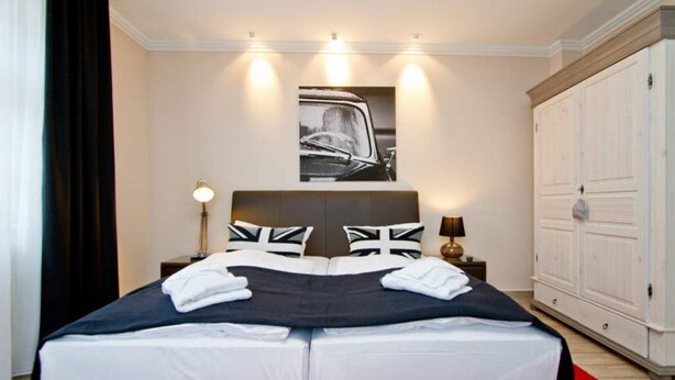 A double bed with a black and white duvet, two pillows with Union Jack designs, a red and black throw blanket, and a white towel folded on the bed.