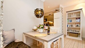 A modern kitchen with a dining table, a hanging pendant light, and a bookshelf.