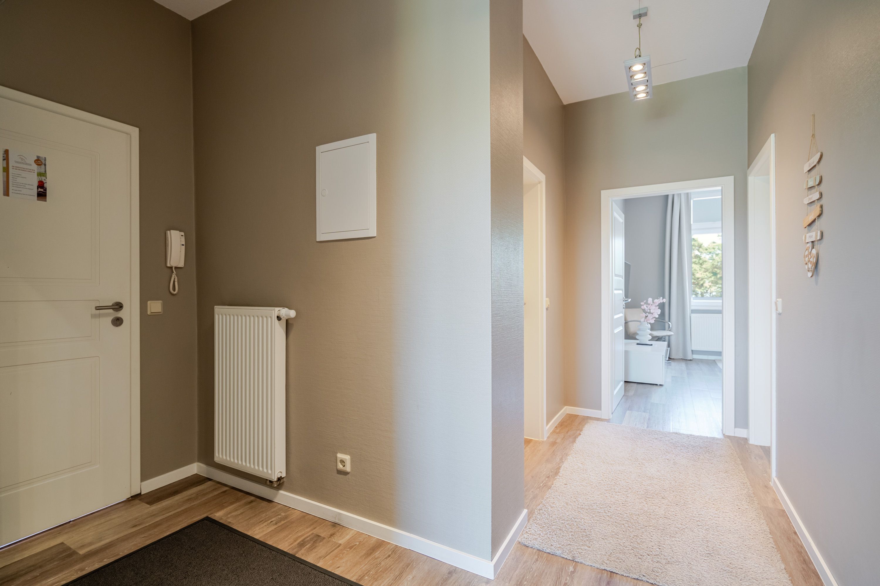A hallway with a radiator, a white door, and a light switch on the wall.