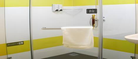 A glass-enclosed shower stall with a white towel hanging on a rack, a handheld showerhead, and a soap dispenser on the wall.