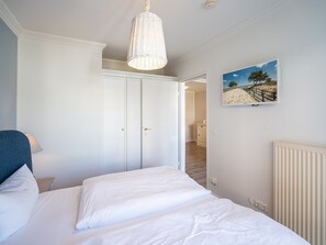 A bedroom with a bed, a hanging light fixture, a painting, and a door leading to another room. - Seehof Bansin, App. 1.14 (Heringsdorf)