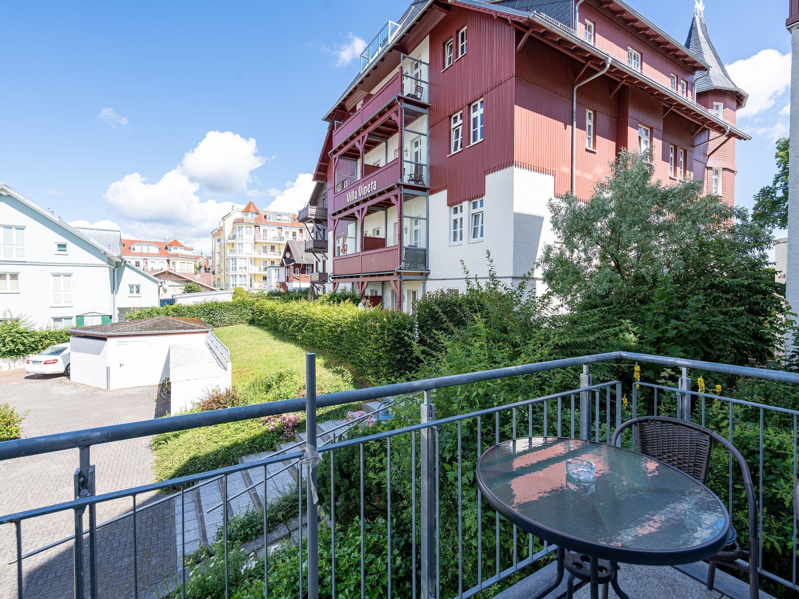 Ein rotes Gebäude mit Balkonen, einem Garten und einem Tisch mit Stühlen auf einem Balkon.