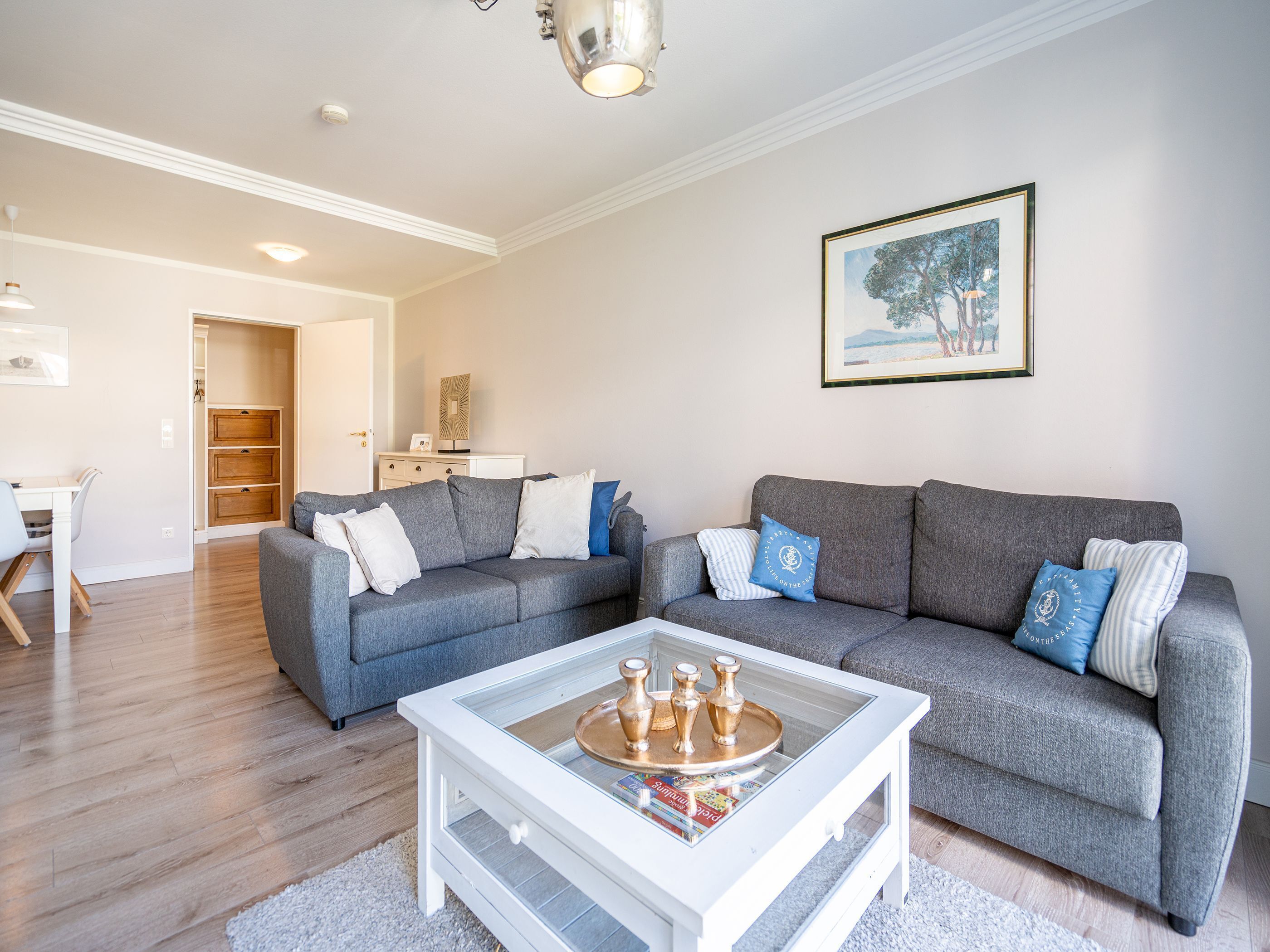 A modern living room with a grey sectional sofa, a glass coffee table, and a dining area with a white table and chairs.