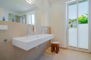 Un bagno moderno con un lavandino capiente, due rubinetti, uno specchio e un piccolo sgabello.