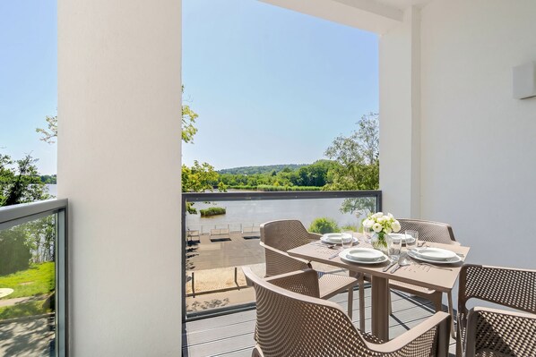 A balcony with a table set for dining, overlooking a body of water and greenery.