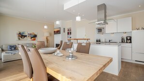 Une cuisine moderne avec des meubles blancs, un îlot central et un coin repas comprenant une table et des chaises en bois.