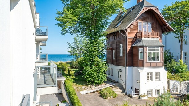 A wooden house with a balcony, a stone wall, and a view of the sea.
