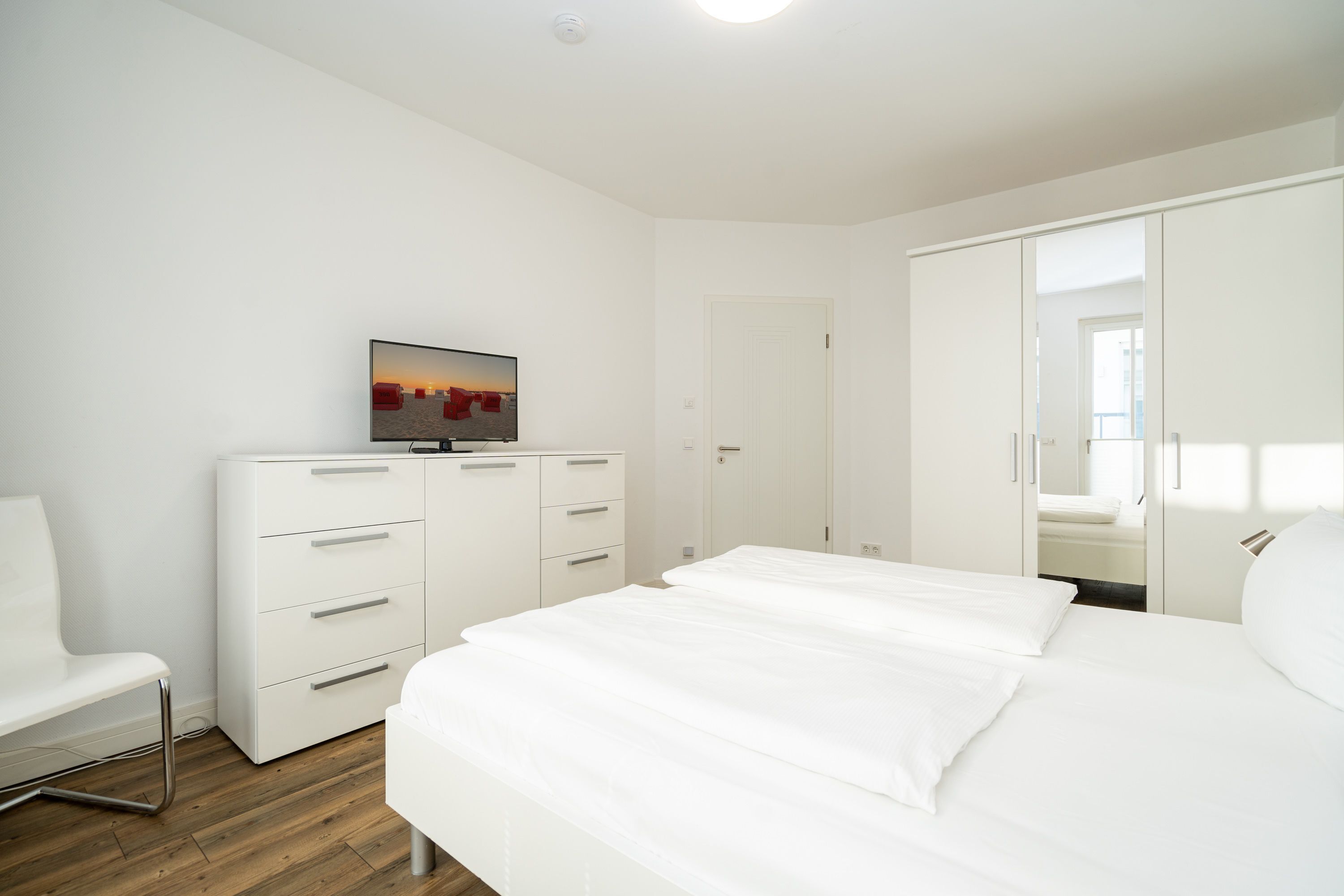 A modern hotel room with a bed, a TV, a wardrobe, and a desk.