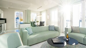 A modern living room with a sofa, a coffee table, and a dining area in the background.