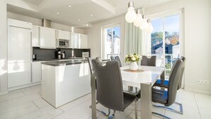 A modern kitchen with white cabinets, a central island, and a dining area with a white table and chairs.