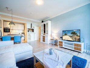 Ein modernes Wohnzimmer mit Flachbildfernseher, ein Essbereich mit blauen Stühlen, eine Küche mit weißen Schränken und eine Treppe, die zu einer weiteren Ebene führt.
