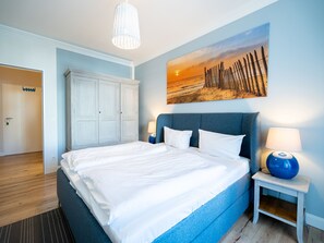 Ein Schlafzimmer mit einem großen Bett, einem Kleiderschrank, einem Bild mit Strandmotiv und einer Lampe auf einem Nachttisch.