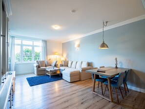 Una sala moderna con un juego de sofá, una mesa de comedor con sillas, un tapete azul y un ventanal con cortinas.