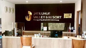 A reception area with a dark wall and a sign for Jatiluhur Valley & Resort. There are two wooden chairs and a counter with a computer and some items on it. - Jatiluhur Hotel Valley & Resort (Purwakarta)