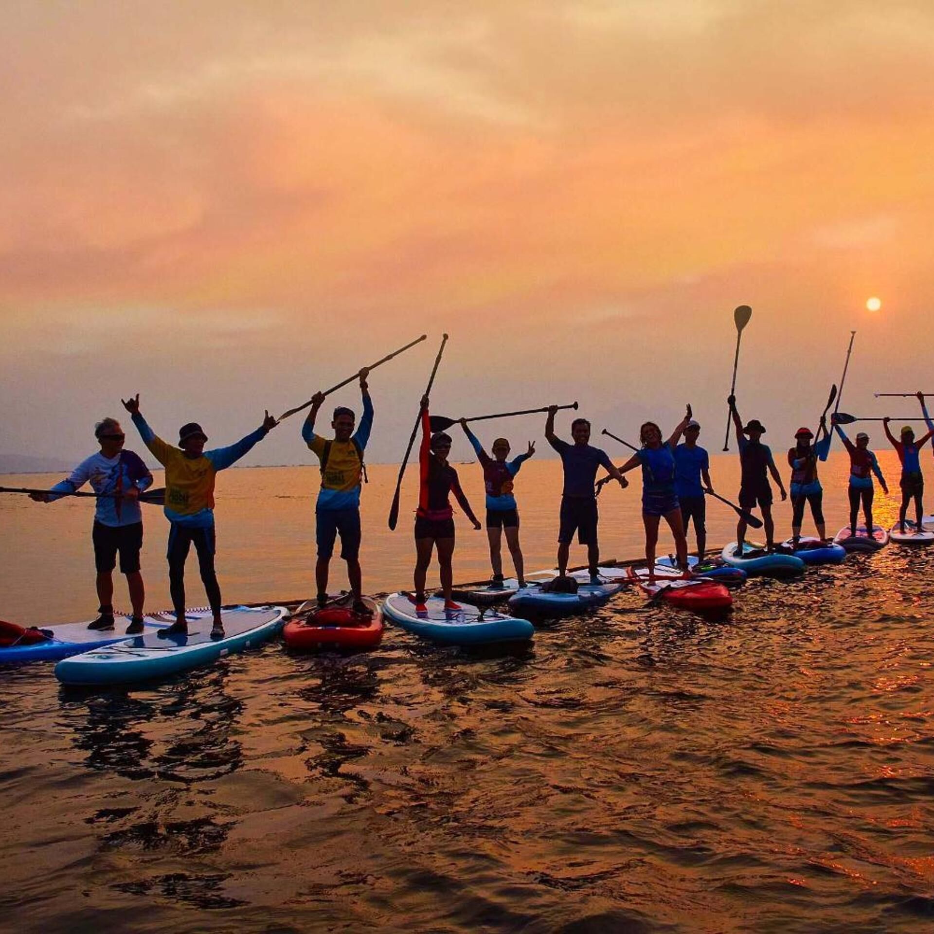 A group of people paddleboarding on a calm body of water during sunset.