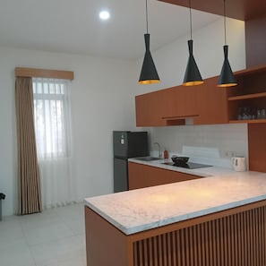 Uma cozinha moderna com bancada de mármore, armários de madeira, forno embutido e iluminação pendente.