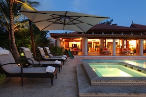 A poolside area with lounge chairs and umbrellas, a pool, and a building with an open patio.