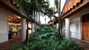 Un patio con jardín central, palmeras y un edificio con suelo de baldosas y vigas de madera.