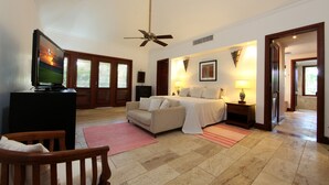 Habitación de hotel con cama, televisión, ventilador de techo, una silla de madera y un tapete rojo.
