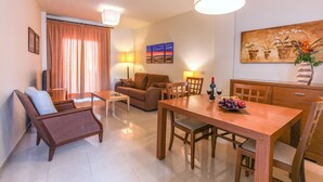 A living room with a sofa, a dining table, and a coffee table. There is a painting on the wall and a lamp on the table. - Marina Turquesa - Apartment 2 bedrooms 2 bathrooms and terrace garden views (Nerja)