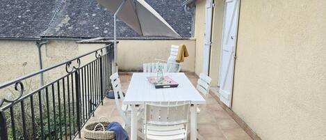 Un patio con una mesa y sillas blancas, un paraguas grande y una cesta.