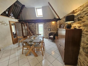 Un coin repas avec une table et des chaises en bois, un escalier, un mur en pierre et un meuble avec une lampe.