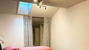 Een slaapkamer met een bed, kussens, een houten hoofdbord, een dakraam en gordijnen.