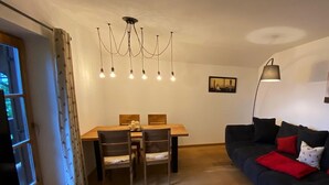 Een eethoek met een houten tafel en stoelen, een kroonluchter en een donkerblauwe bank met rode kussens.