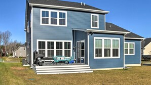 A two-story house with a covered porch, large windows, and a visible outdoor grill area. - Modern Lewes Home w/ Deck, Grill + Pond View! (Lewes)