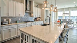 Une cuisine spacieuse avec des meubles blancs, un grand îlot central et des luminaires suspendus.