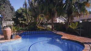 A swimming pool with a blue mosaic tile edge, surrounded by a brick patio and various plants.