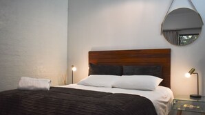 A neatly made bed with a wooden headboard, a round mirror on the wall, and two bedside lamps.