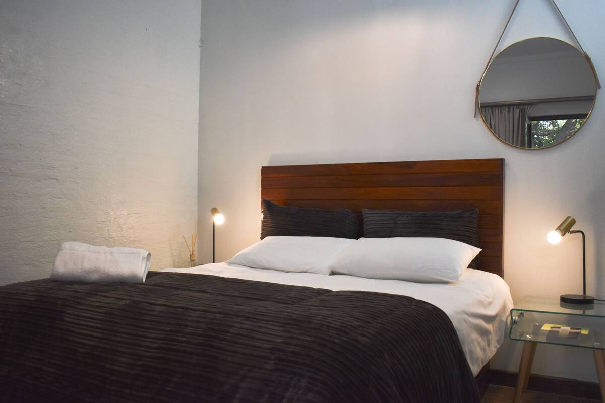 A neatly made bed with a wooden headboard, a round mirror on the wall, and two bedside lamps.