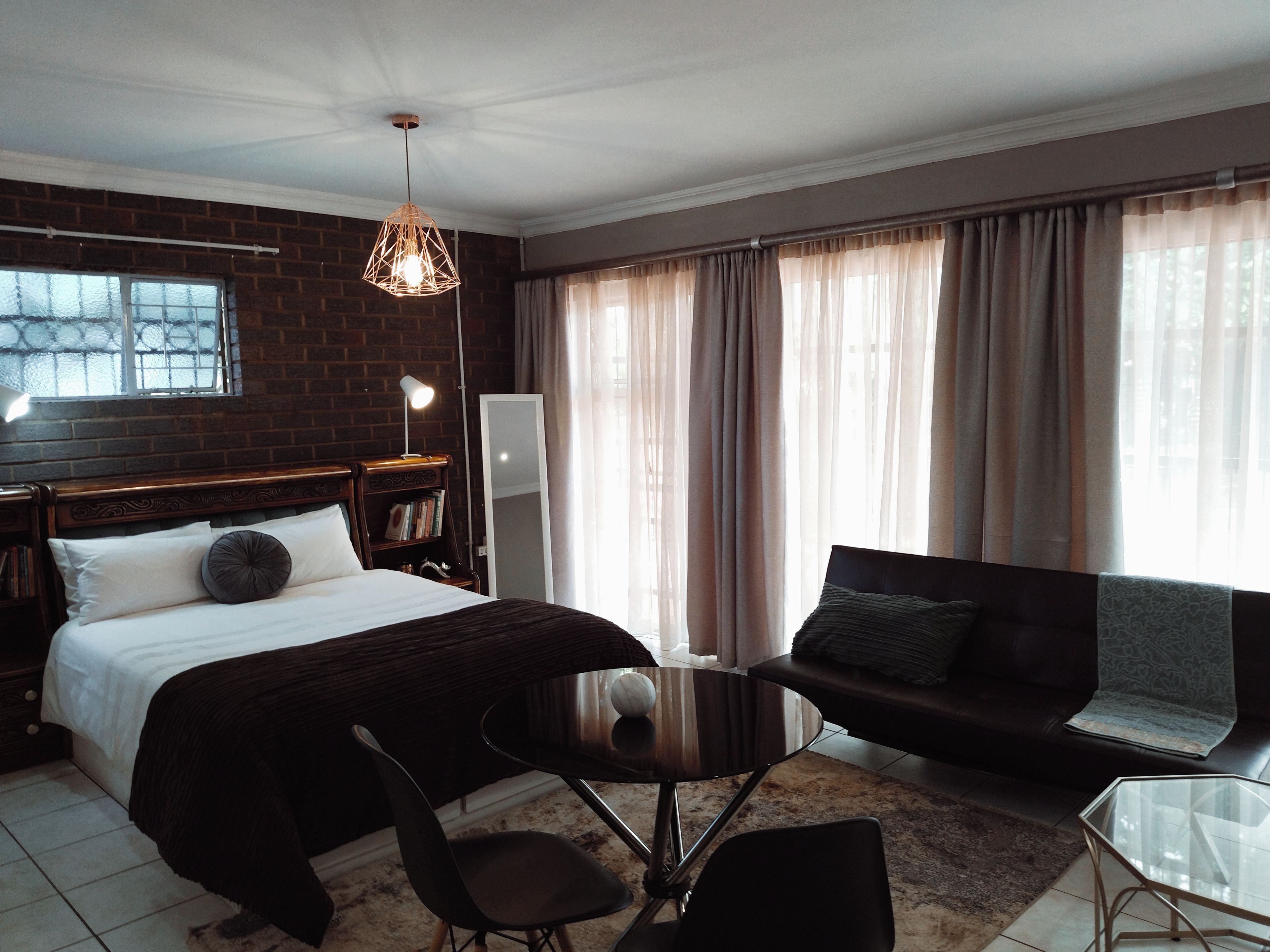 A hotel room with a bed, a sofa, a small table, and a mirror.