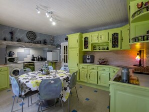 Uma cozinha com armários verdes, uma mesa de jantar com toalha de mesa florida e diversos eletrodomésticos.