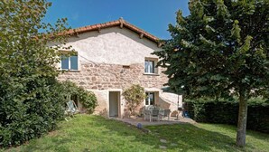 A stone house with a garden, a patio with a table and chairs, and a tree.